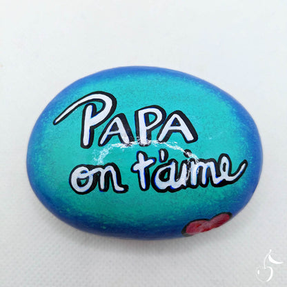 Galet avec un fond de dégradé de bleu, écrit dans son centre "Papa on t'aime"