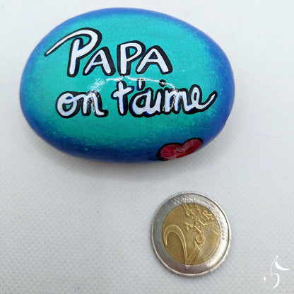 Galet avec un fond de dégradé de bleu, écrit dans son centre "Papa on t'aime"