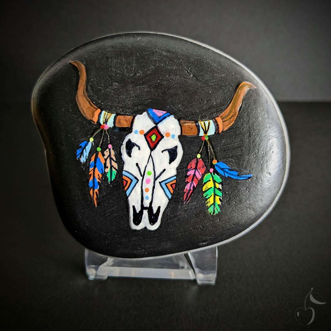 Découvrez le galet 'Skull' de la collection Indien, un hommage à la culture amérindienne. Ce galet représente un trophée indien, un crâne de taureau décoré de plumes colorées. 