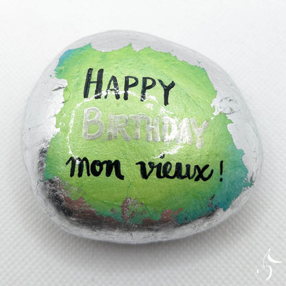 Galet peint de couleur vert/bleu aux bords en feuille argentée. Sur le galet est écrit : "Happy Birthday mon vieux".