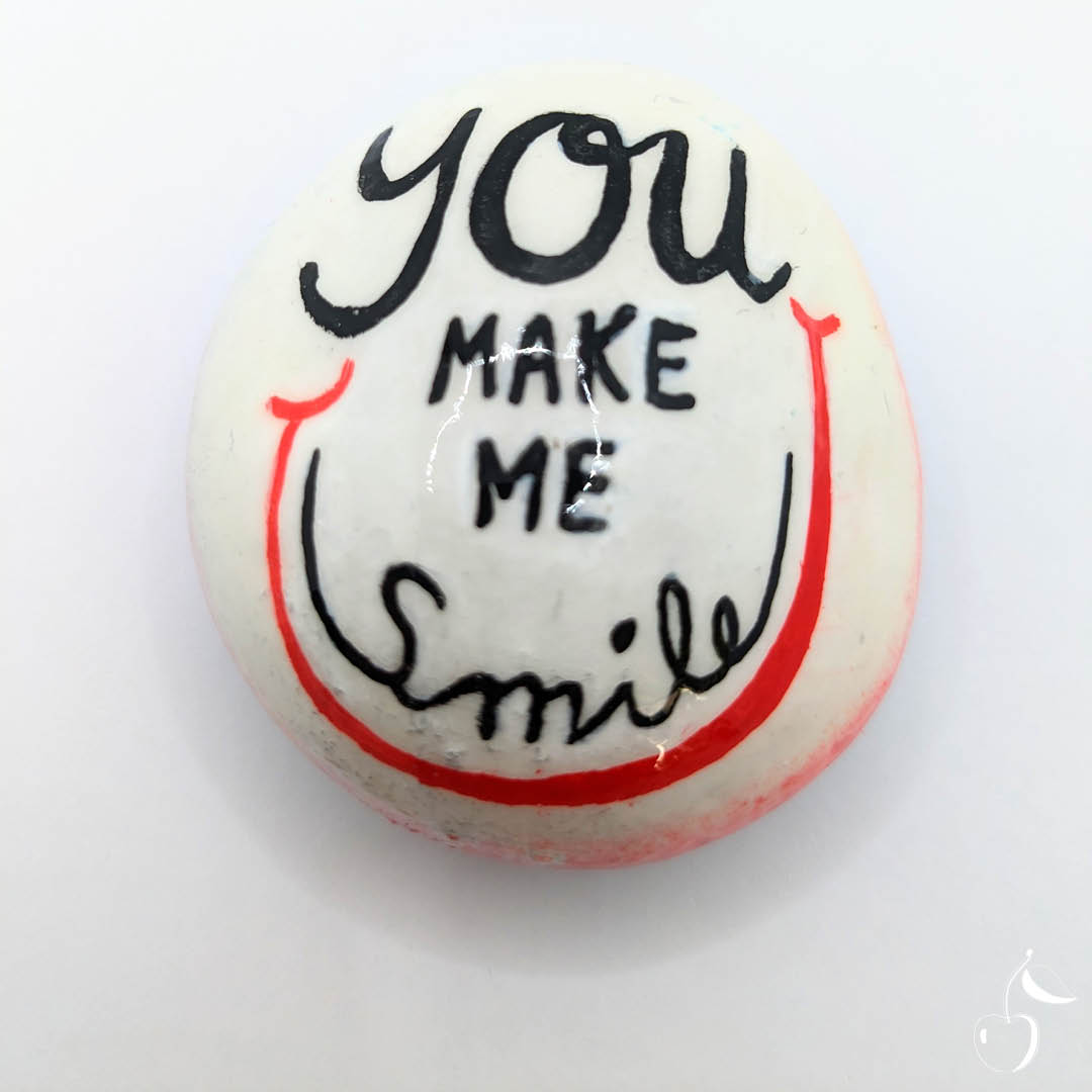 Galet blanc et rouge orné d'un grand sourire. Inscription "You make me smile" en son milieu.