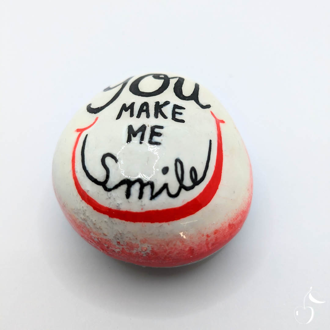 Galet blanc et rouge orné d'un grand sourire. Inscription "You make me smile" en son milieu.