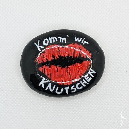 Galet noir avec empreinte d'une bouche rouge et le texte en blanc "Komm' wir knutschen!"