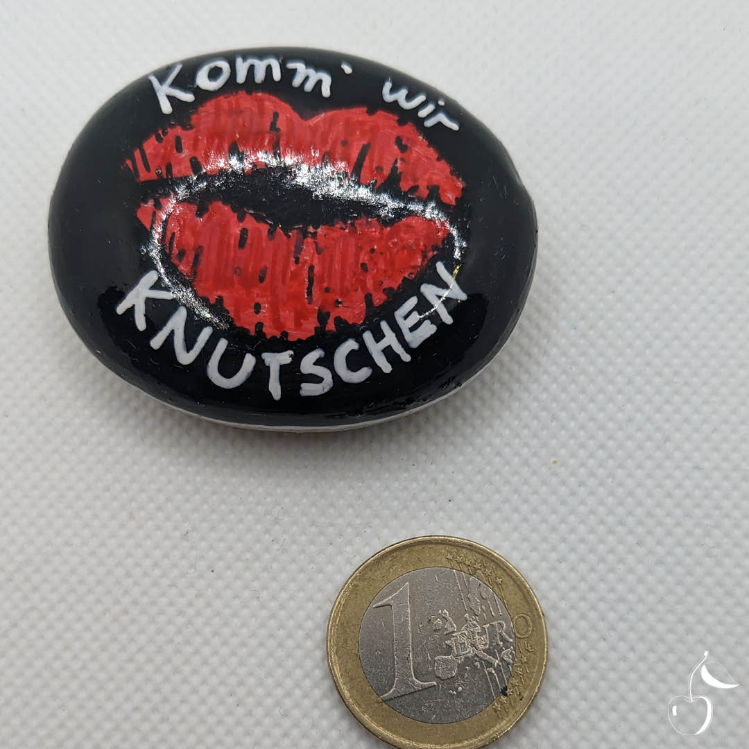 Galet noir avec empreinte d'une bouche rouge et le texte en blanc "Komm' wir knutschen!"
