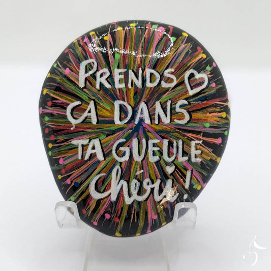 Image d'un galet peint sur fond noir orné de traits de tous les couleurs tel un feu d'artifice. Inscription "Prends-ça dans ta gueule chéri."